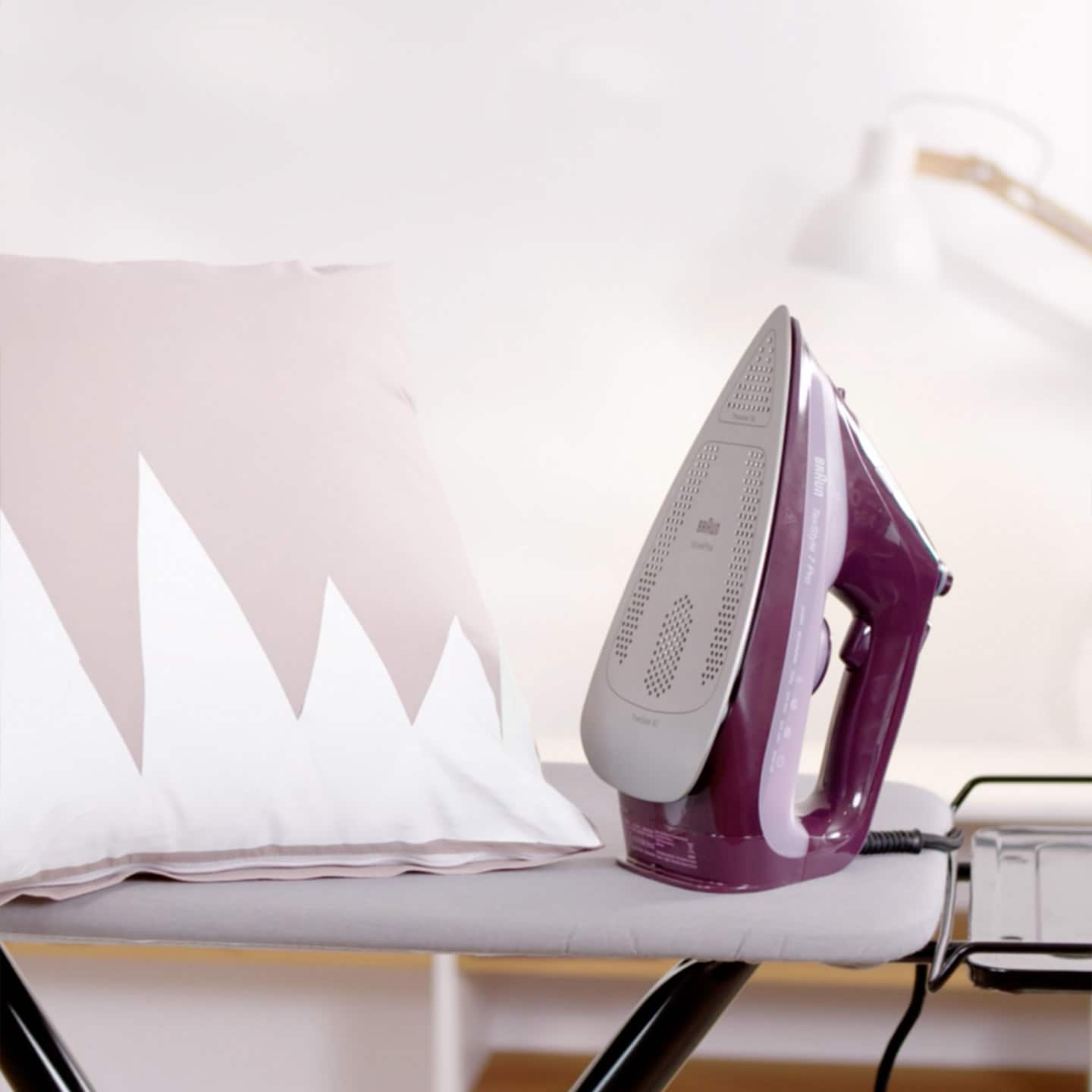 A purple iron placed on a table next to a pillow.