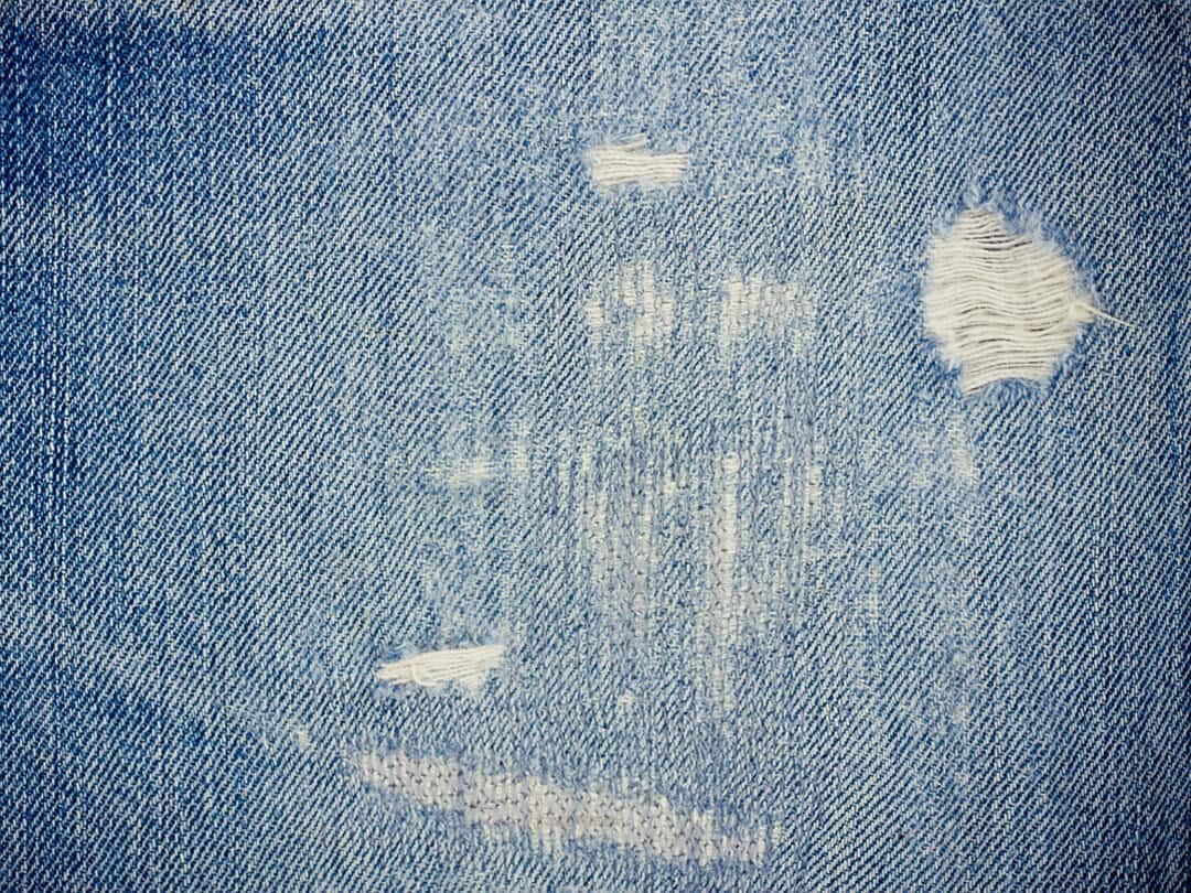 Close-up of distressed blue jeans with frayed holes, showcasing the worn texture.