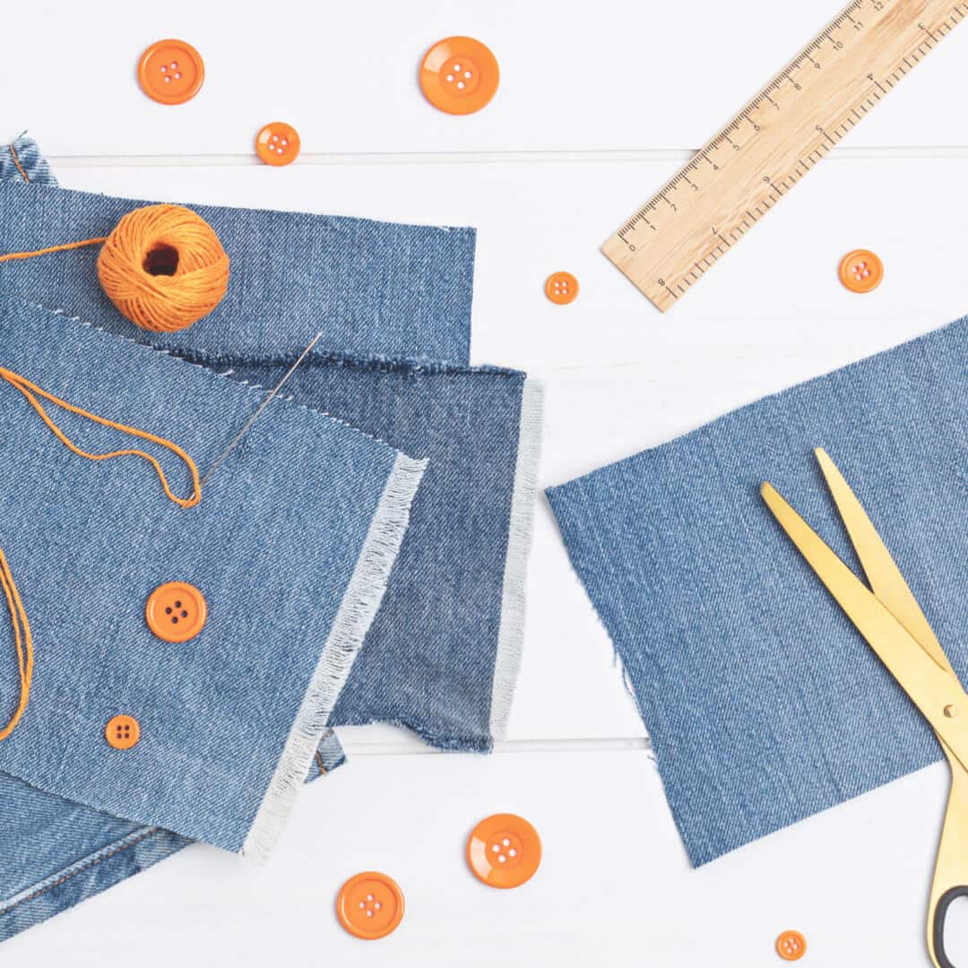 A pair of scissors, jeans, and orange buttons laid out on a table.