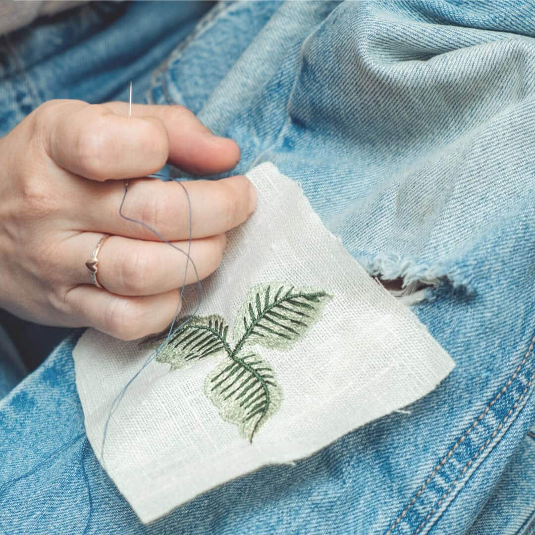 A person sewing a leaf onto a pair of jeans