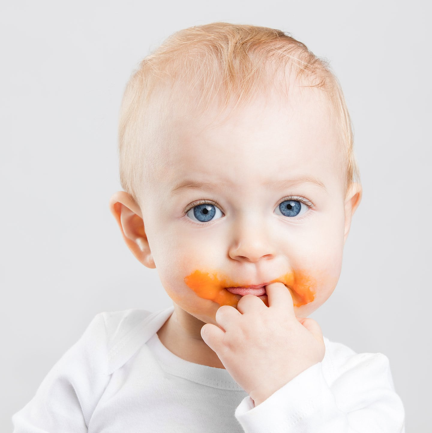 Baby with big blue eyes and carrot puree around his mouth