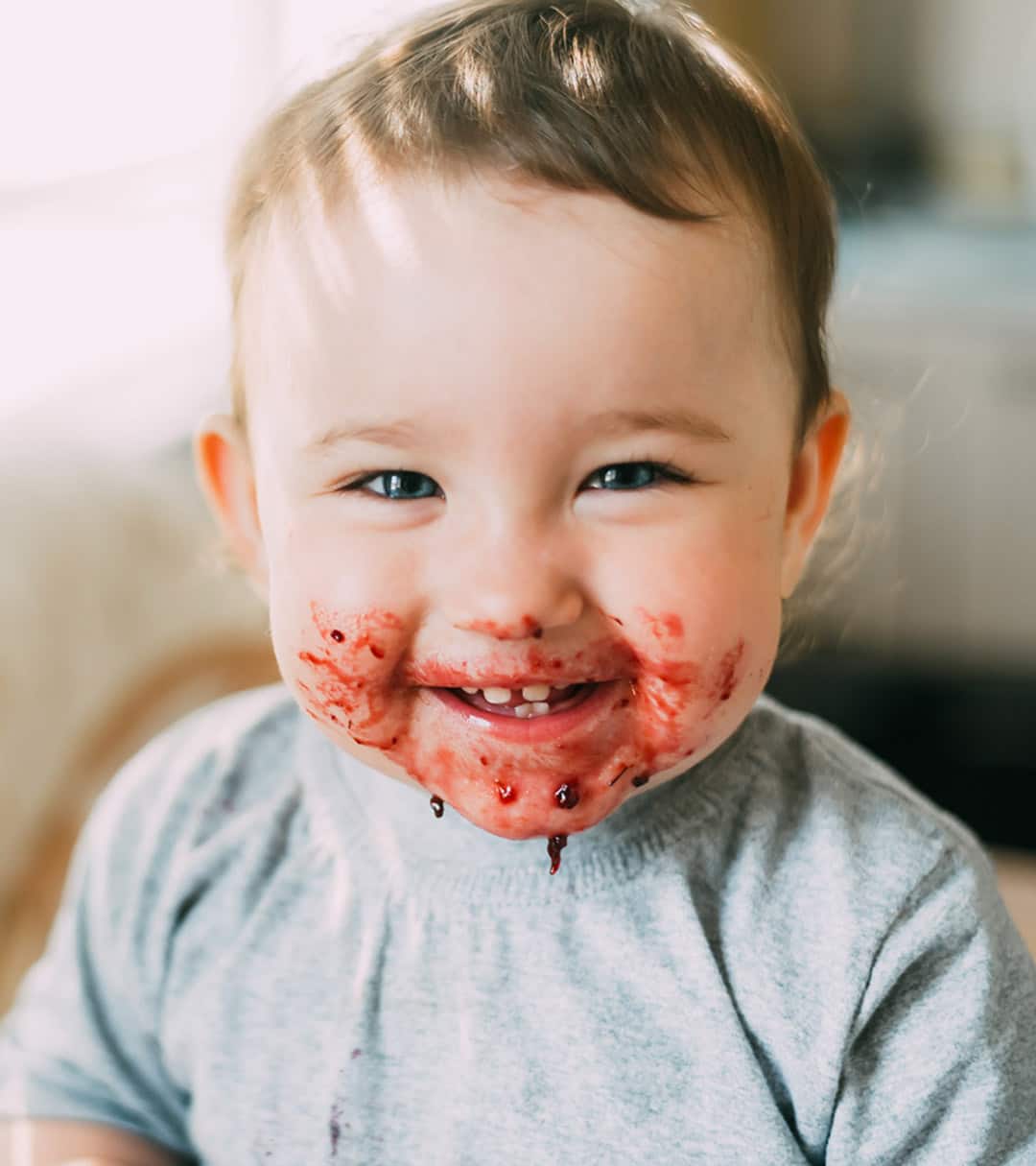 Laughing baby with red fruit pulp around his mouth