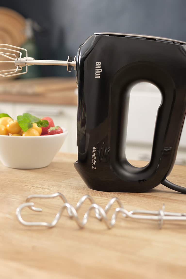 Black MultiMix 2 hand mixer standing upright on table next to a plate of cupcakes