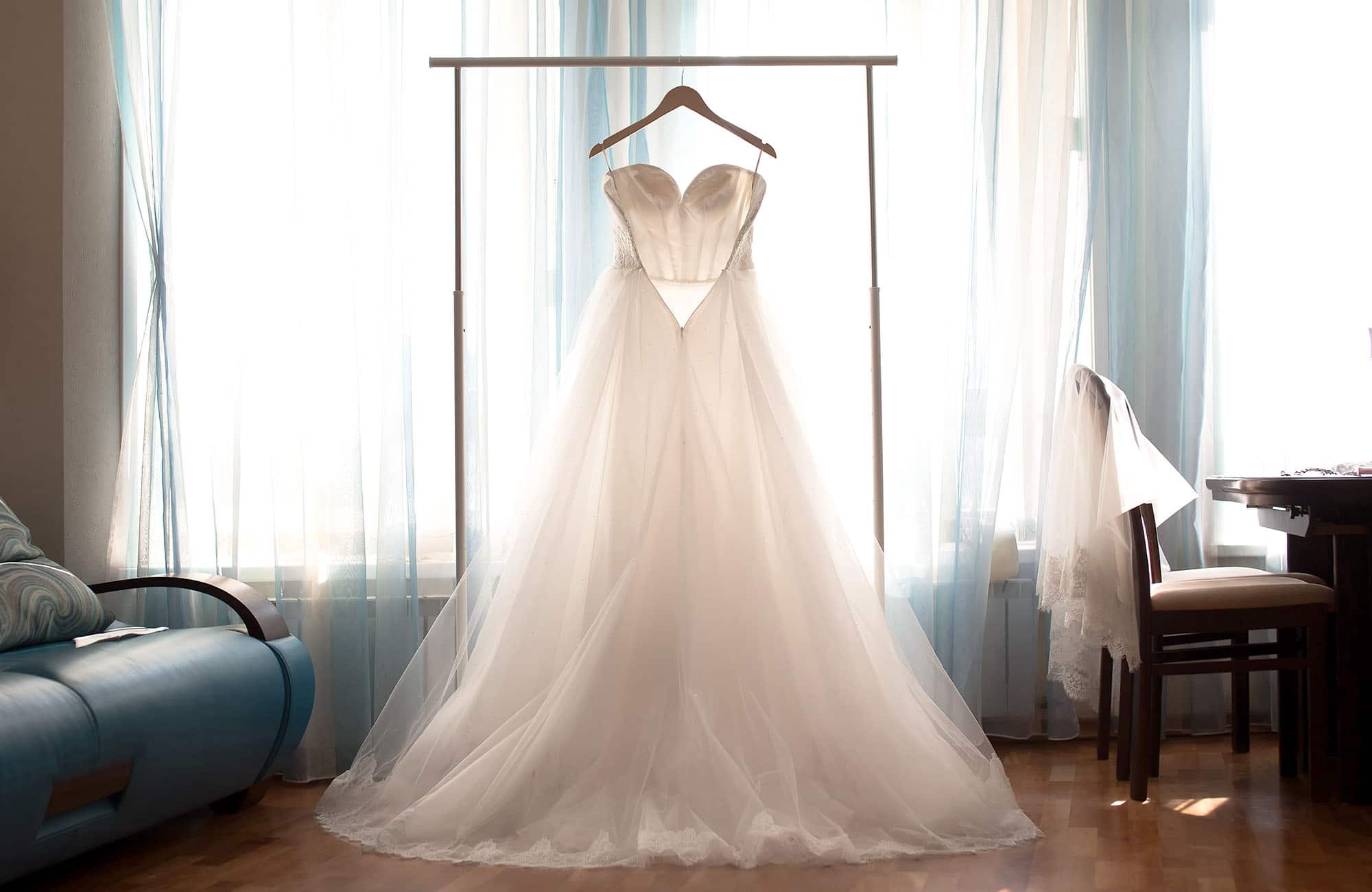 Tiulowa suknia ślubna wisząca na wieszaku na tle okna